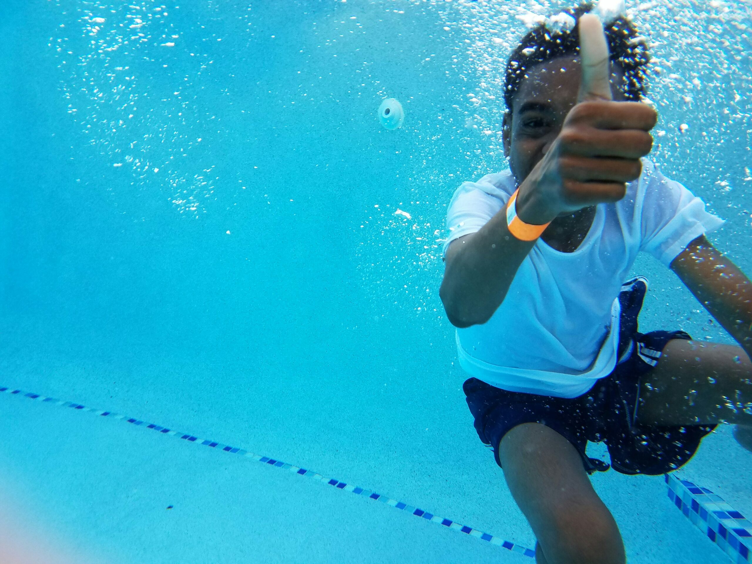 Jongen zwemt onderwater en steekt zijn duim op boven water